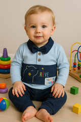 A baby sitting on the floor wearing a blue and navy pants set with a colorful character print and bow tie detail.